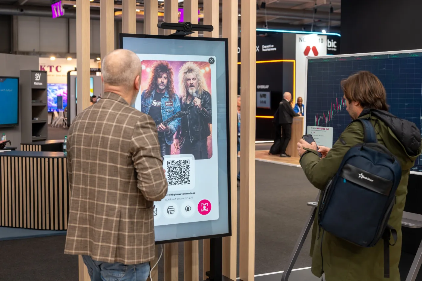 Two visitors at the iiyama stand at ISE 2026 look at their result: two glam rock musicians, one in an iiyama T-shirt.